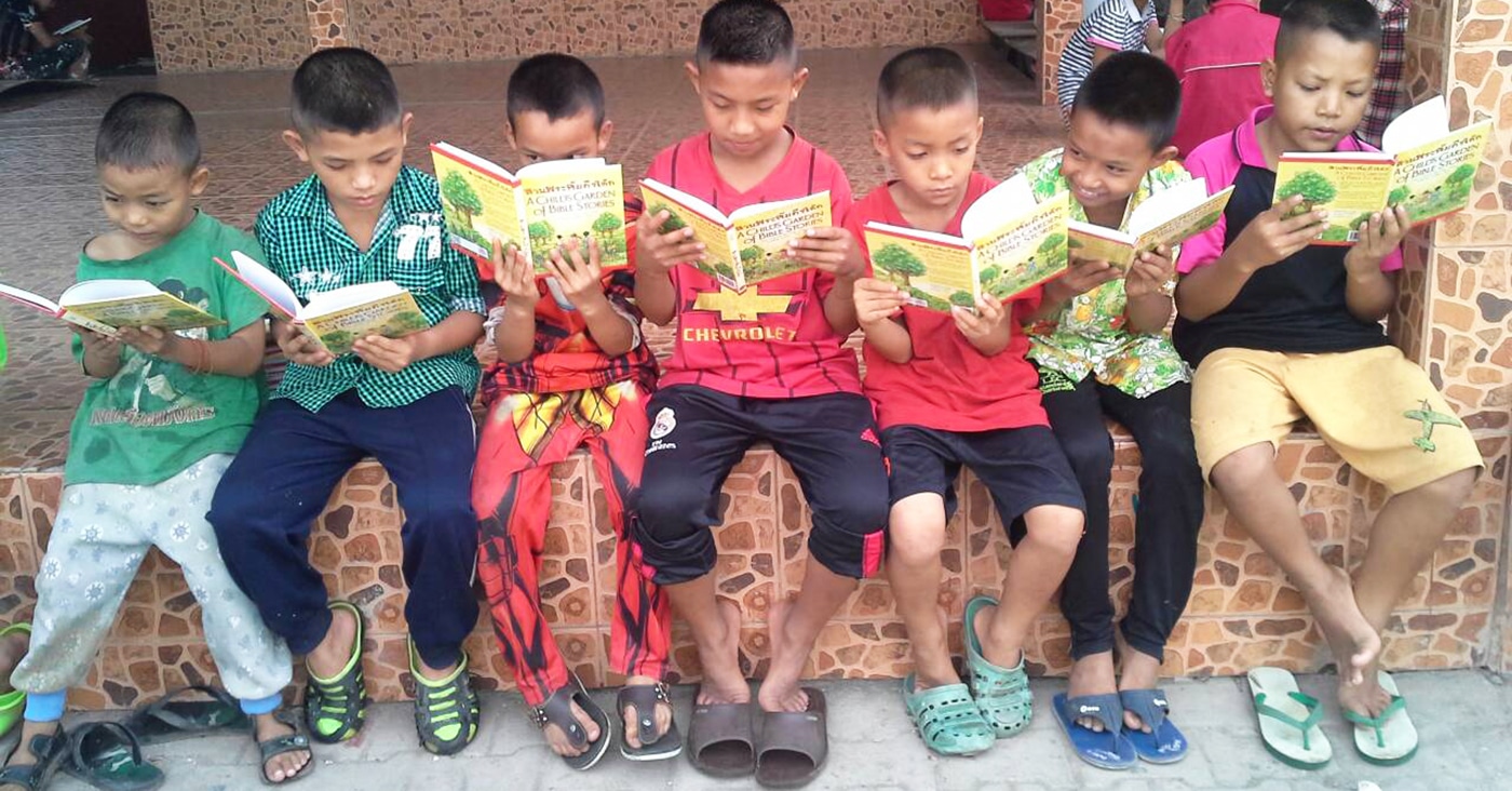 Thai School Children Sitting In A Row Reading A Child's Garden of Bible Stories