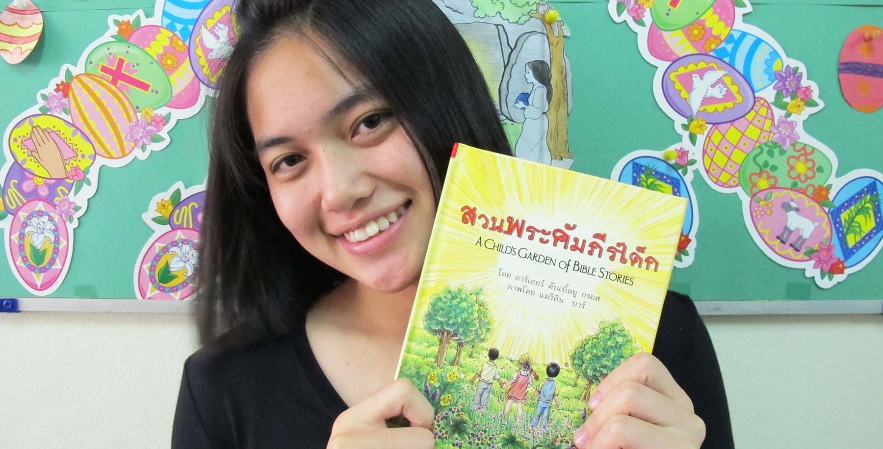 Thai Teen Holding Up A Child's Garden of Bible Storybooks